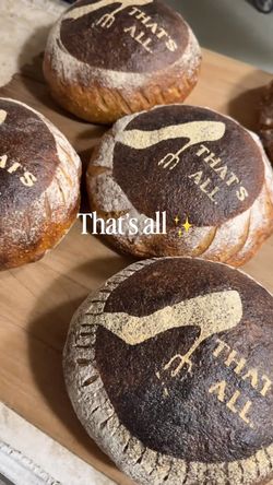 Round loaves of bread with a dark crust marked 'That's All' on a wooden surface at Breads Bakery – Union Square.