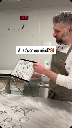 A bakery staff member illustrates ideas or plans on a whiteboard, with bakery items and sketches visible.