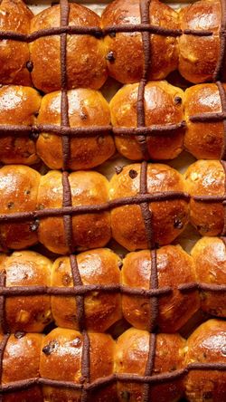 Golden brown hot cross buns with a chocolate cross pattern baked and arranged in rows at Breads Bakery