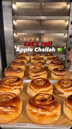 Freshly baked apple challah rolls on a tray inside a bakery oven at Breads Bakery with a golden-brown crust.