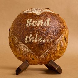 Artisan bread with a heart design, featuring the text 'Send this' on a rustic stand.