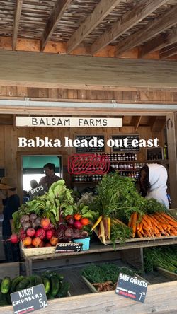 Fresh vegetables including beets, carrots, and cucumbers displayed at a farm market stand with wooden beams overhead.