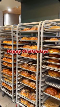 Shelves filled with freshly baked challah bread loaves on metal racks inside Breads Bakery at Rockefeller Center.