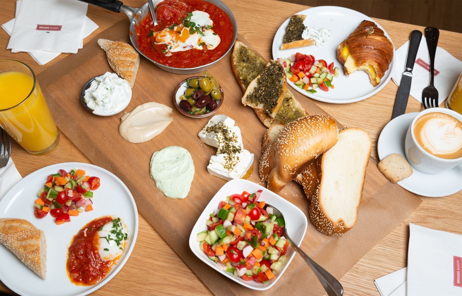 A selection of breakfast items including eggs, salads, pastries, bread, and coffee on a wooden table.