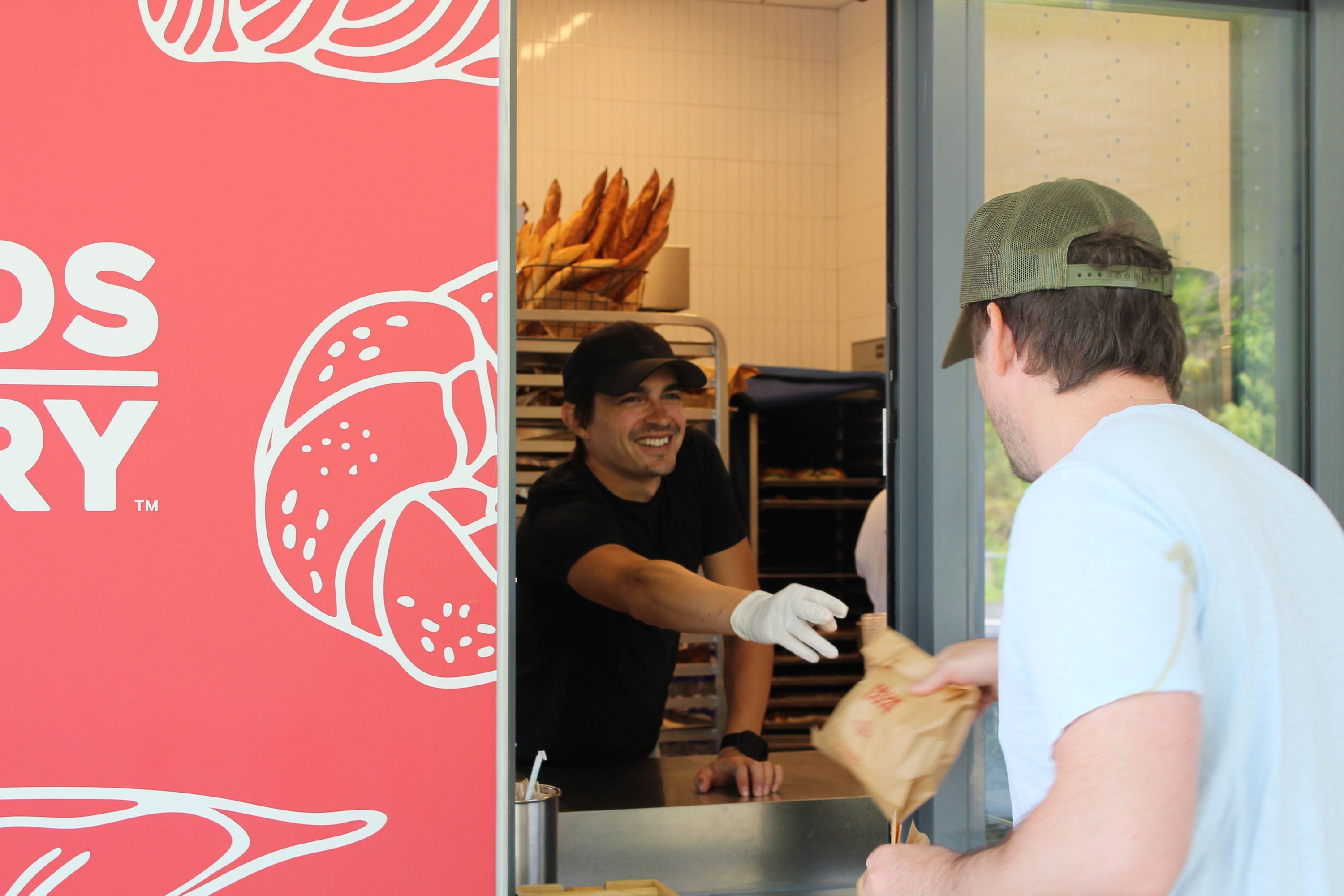 A customer receives a bag from a staff member at Breads Bakery, showcasing pastries and breads.