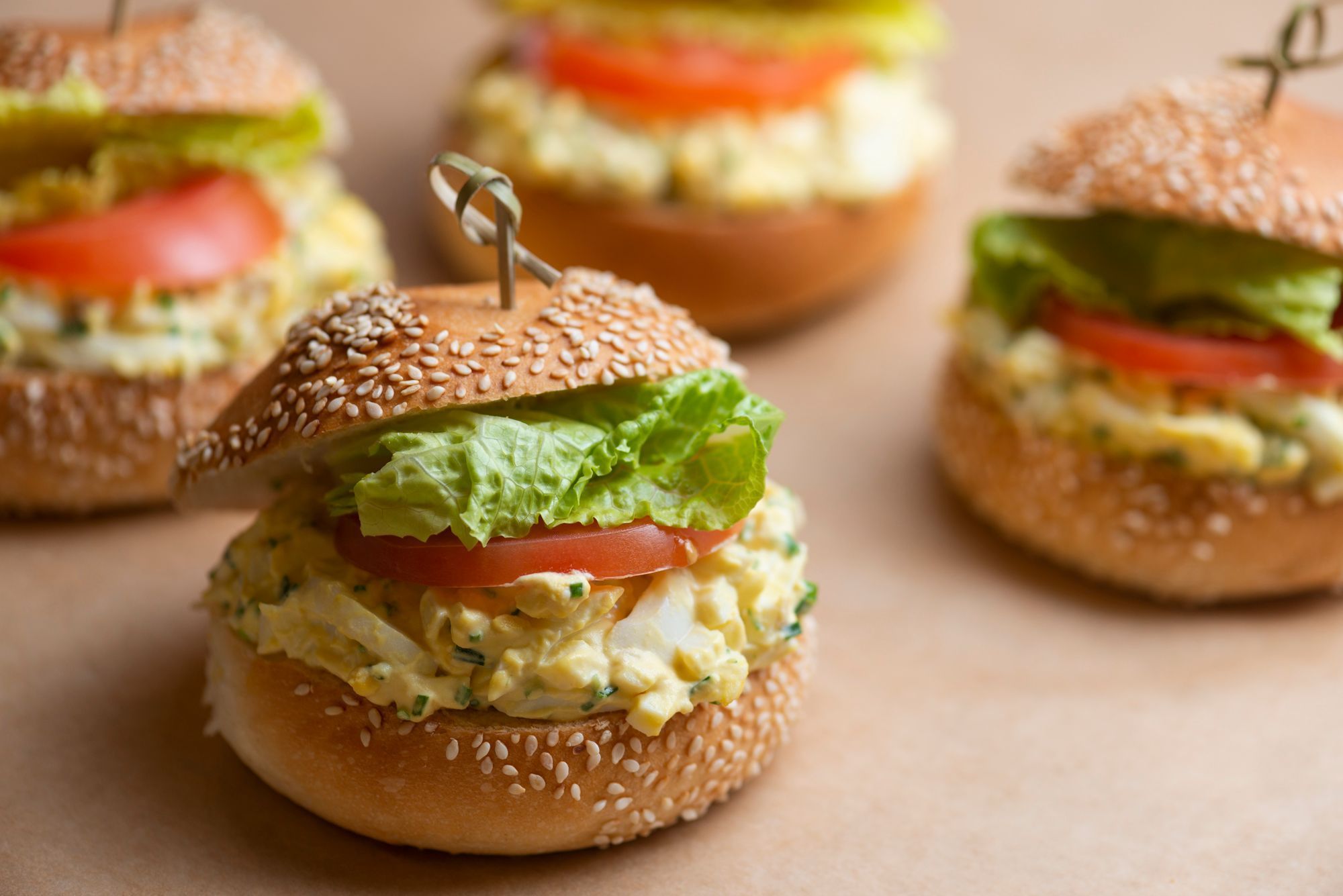Assorted sandwich sliders featuring sesame seed buns, lettuce, tomato, and creamy filling, ideal for lunch.