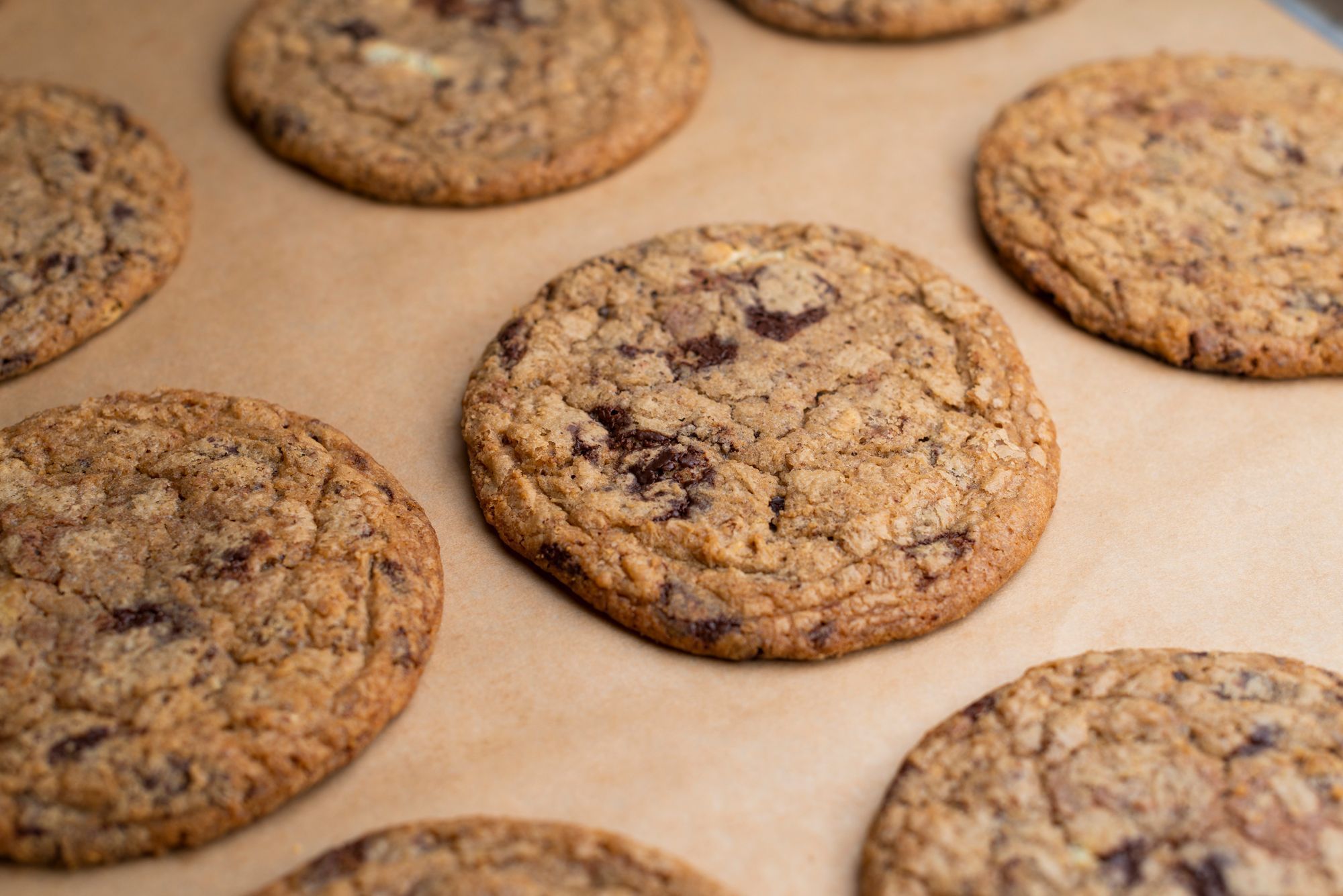 Freshly baked cookies with a golden brown color and chocolate chunks, placed on parchment paper.
