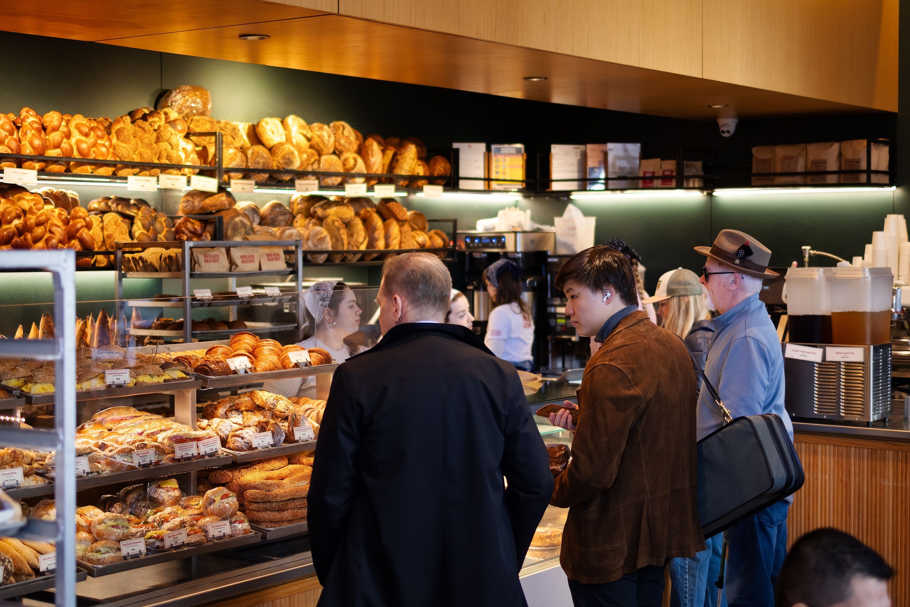 A selection of fresh pastries and breads displayed at Breads Bakery, with customers in line for breakfast or lunch.