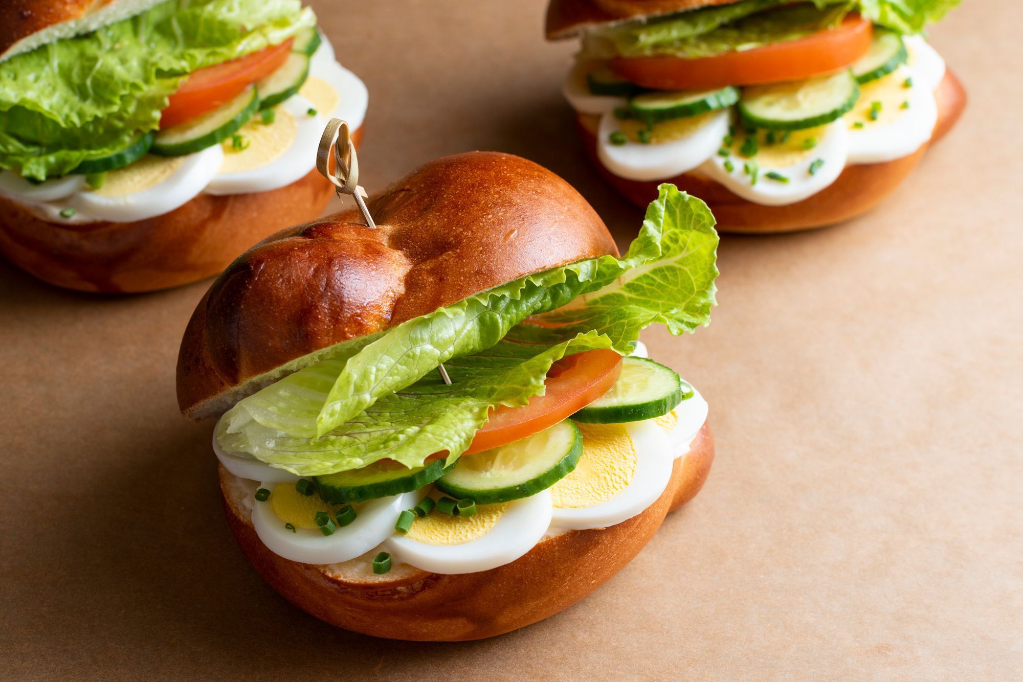 Fresh sandwich with layers of lettuce, tomato, cucumber, and sliced egg on a soft bread bun.