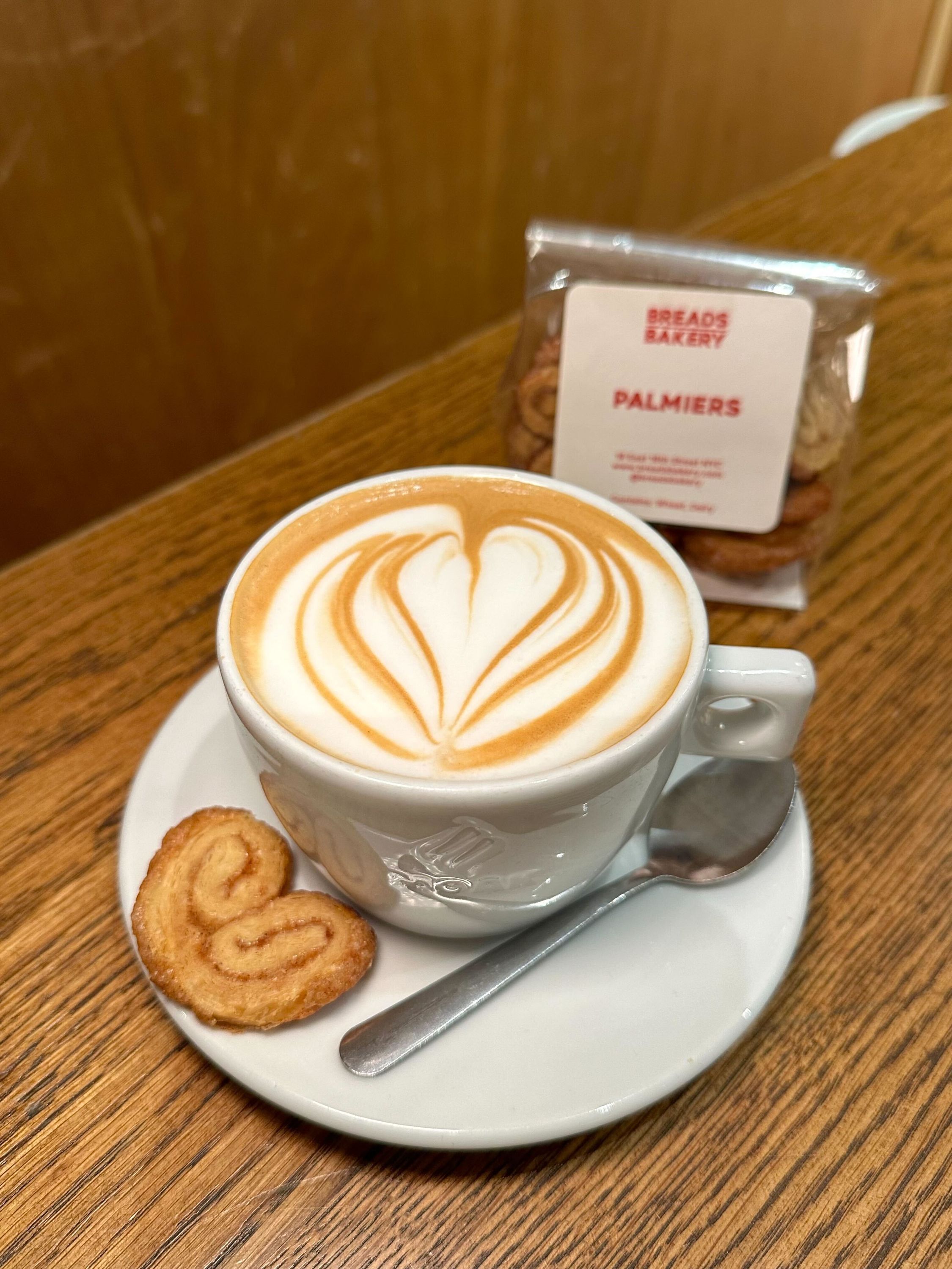 A cappuccino topped with latte art, accompanied by a palmier pastry, at Breads Bakery.