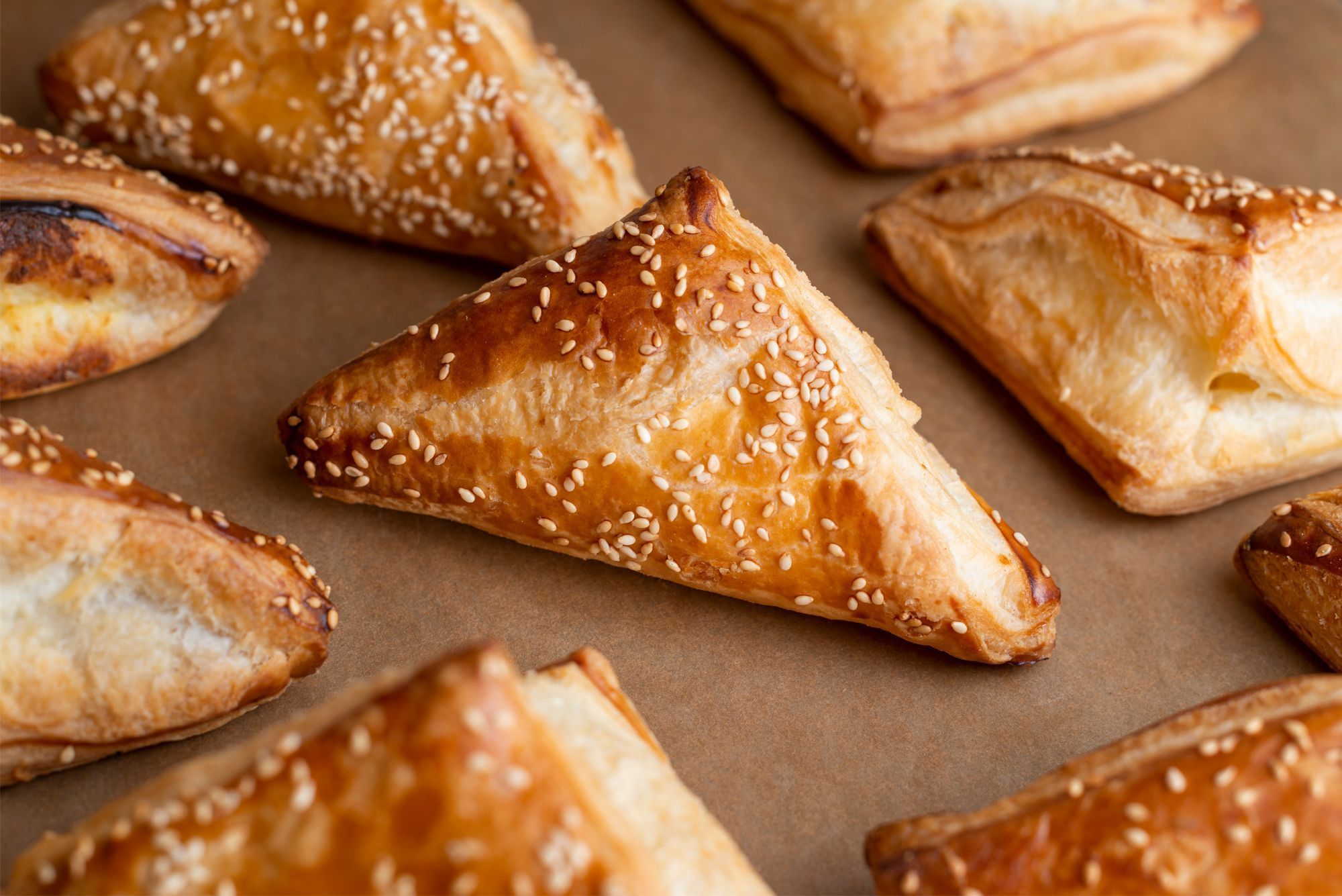 Freshly baked triangle pastries with a golden crust and sesame seeds on top, arranged on parchment.