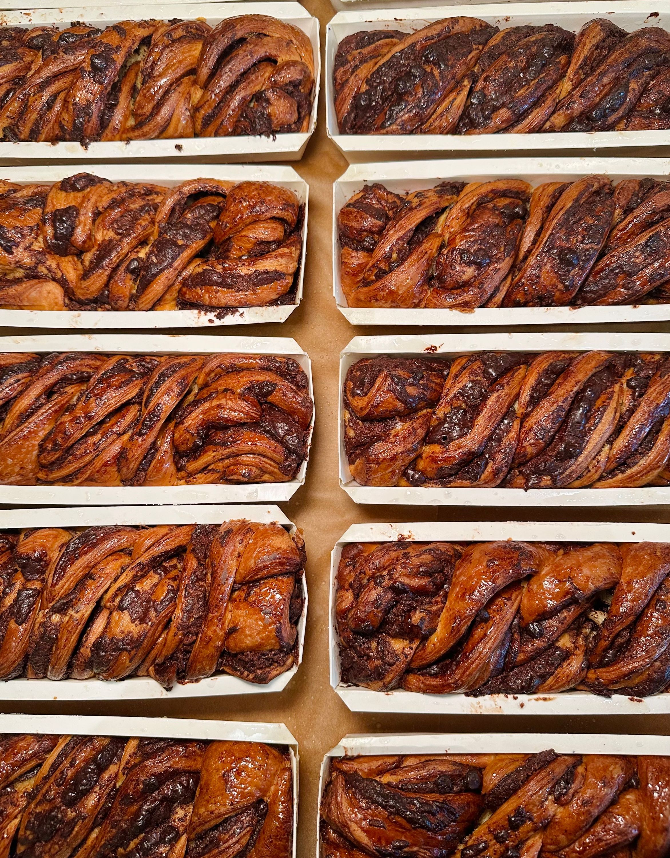 Rows of freshly baked babka loaves, showcasing rich chocolate swirls in a cozy bakery setting.