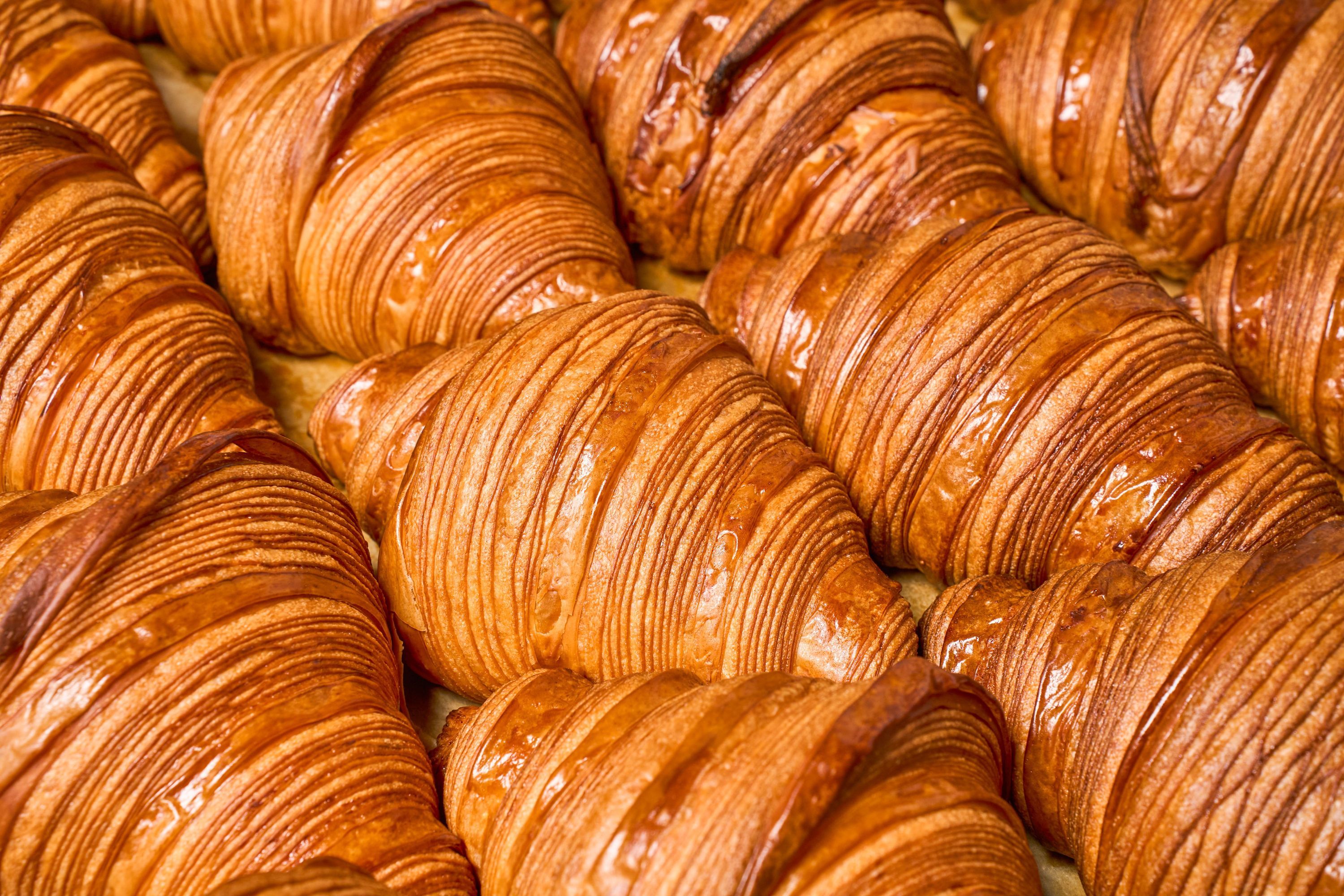 Freshly baked croissants lined up, showcasing golden layers and a flaky texture.