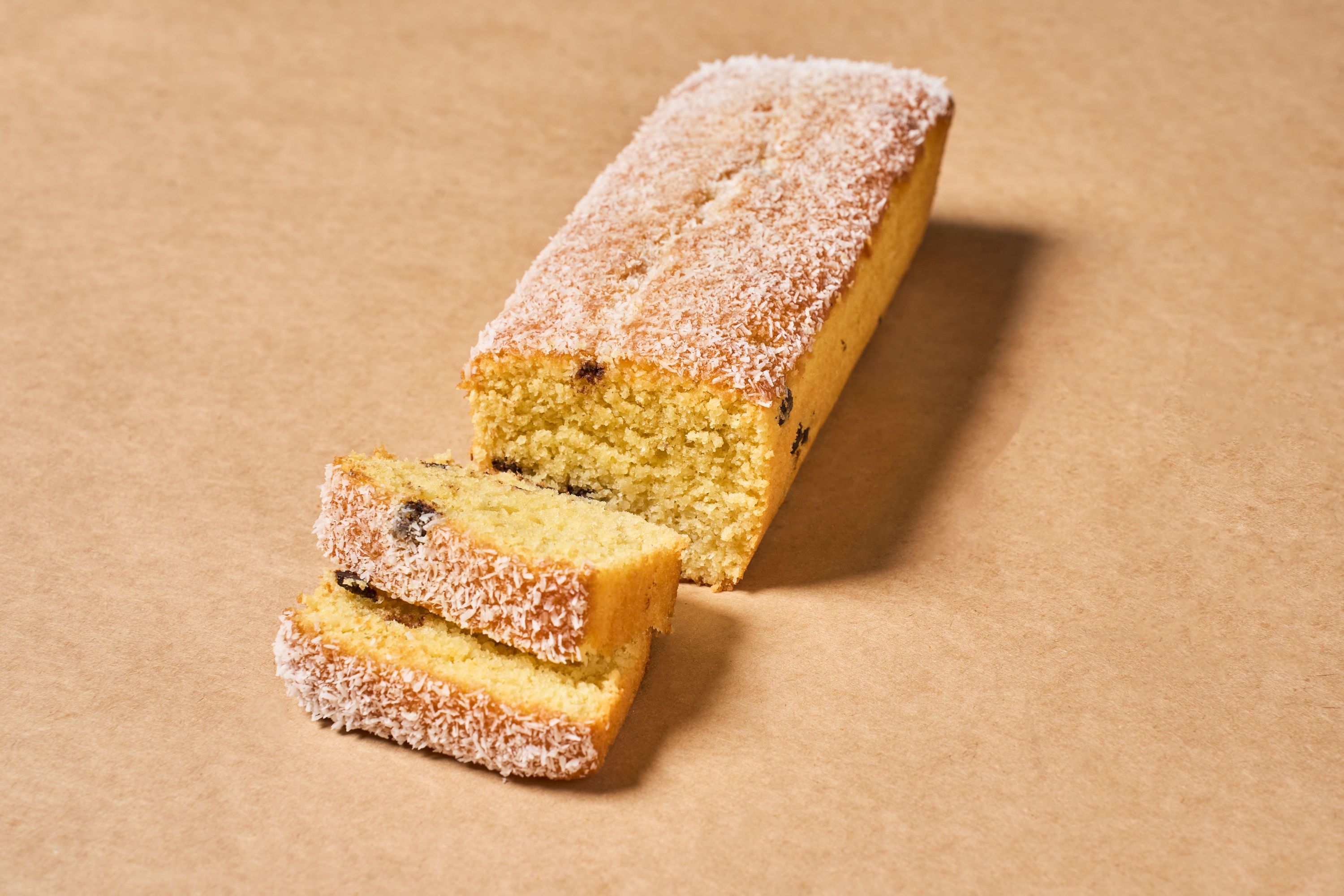 A loaf of coconut-flavored cake with chocolate chips, served with two slices.